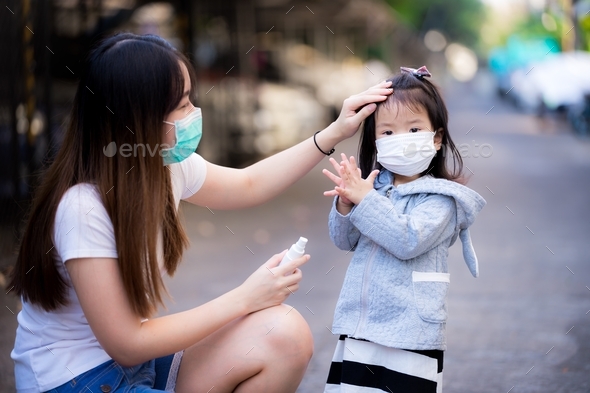 Child washing her hands with alcohol spray that mother sprayed. Protection virus. Family wear masks.