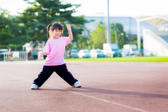 Adorable Asian child girl is exercising at the sports ground.