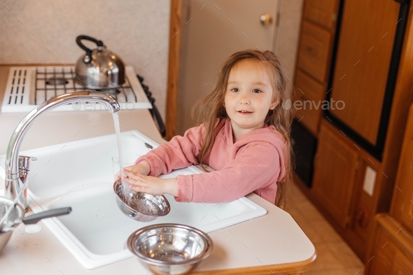 A little girl washes the dishes in the kitchen in the motorhome. Happy childhood concept