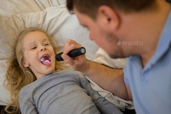 dad checks the throat of his sick child, shines a flashlight so that it is better to see