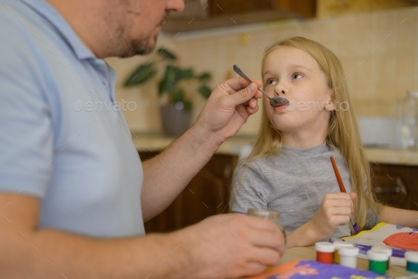 dad feeds honey from a spoon to a sick child at home, who is distracted from the disease by drawing