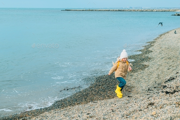 a little girl in rubber delta boots runs happy in the spring along the seashore