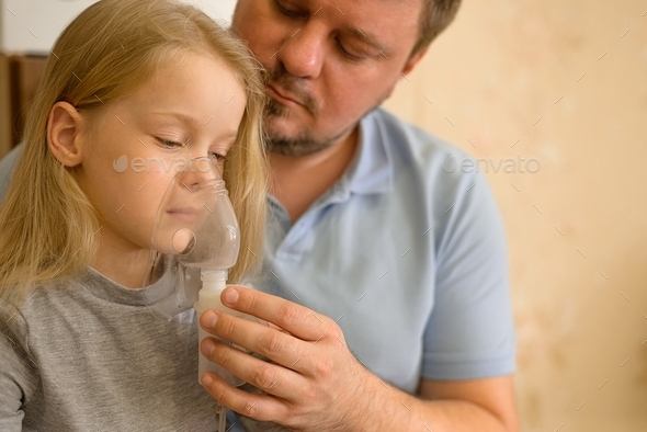 dad helps his sick child do inhalation with a nebulizer at home: he holds a mask from which steam
