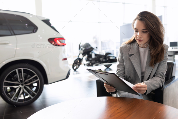 a young woman reads a contract for the purchase of a new car in a car dealership on credit