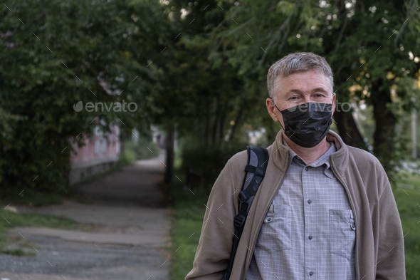 Portrait of a handsome middle-aged man in a protective mask on the street in the city. New rules.