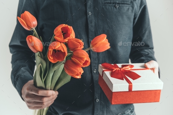 Male hands are holding a bouquet of tulips and a gift box. Congratulations on the holiday.