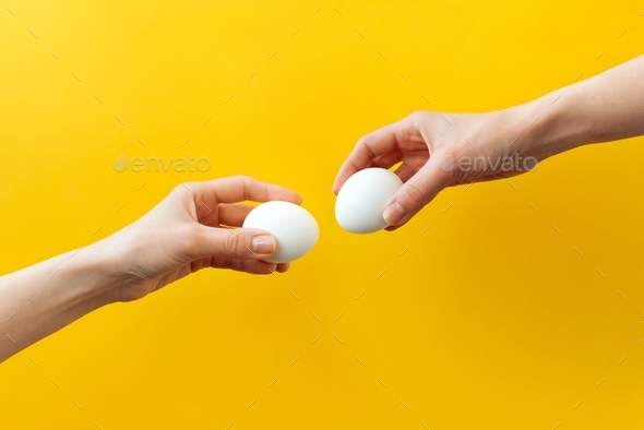 Woman hands holding Easter eggs for knocking on yellow background. Easter celebration or creative co