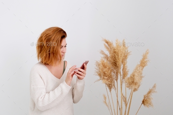 The red hair woman holds the phone in her hands. pampas grass. decorative feather composition for ho - Stock Photo - Images
