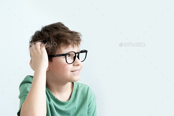 Surprised boy in a green T-shirt and glasses pensive scratches his head. Copy space