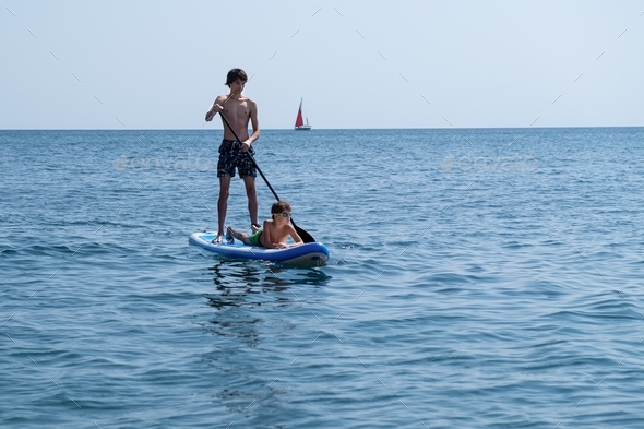 A young sports man with a child sails on a sup in the sea. Healthy lifestyle concept.