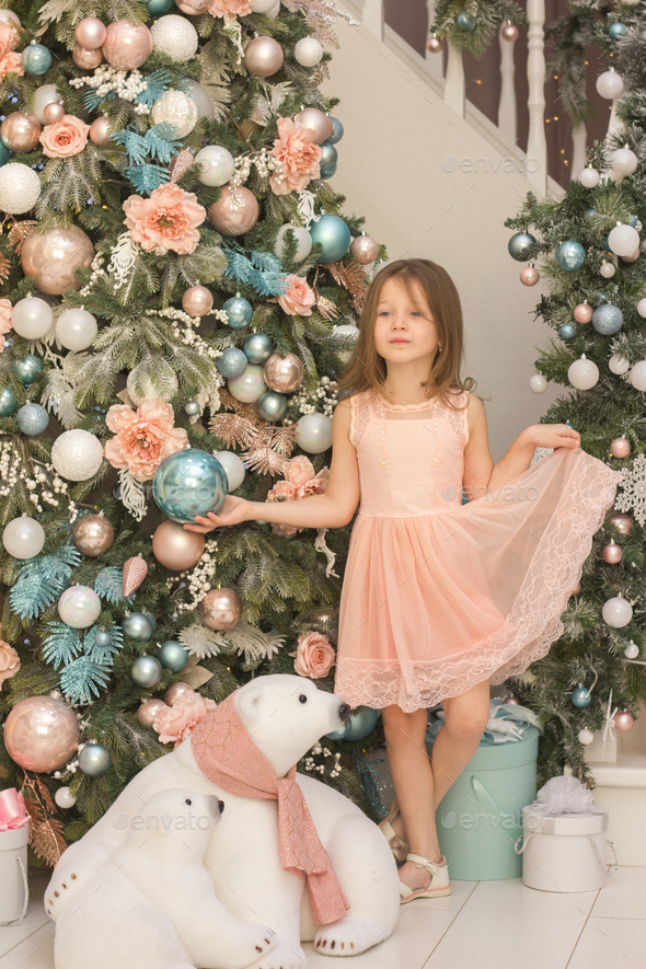 A girl in peach dress depicts a princess at the Christmas tree, holding a dress and a Christmas ball