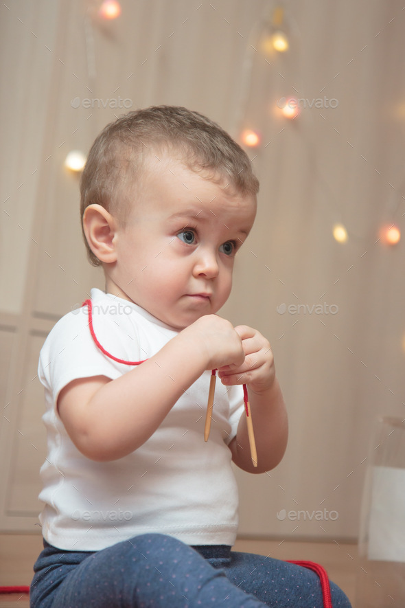 A little kid in a white T-shirt hung a red string around his neck and looks away with a serious face