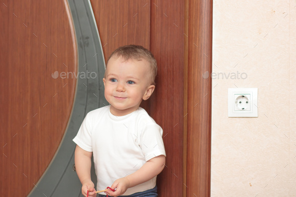 Portrait of a cute baby standing at the door with a smile close-up with a red lace in his hands.