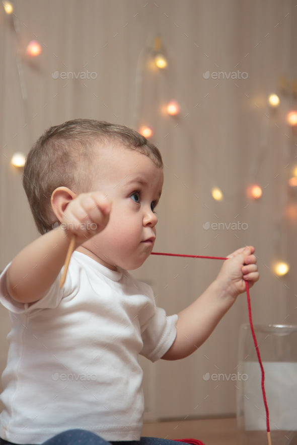A little kid in a white T-shirt hung a red string around his neck and looks away with a serious look
