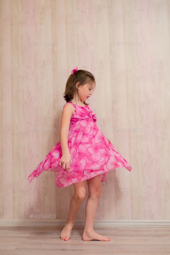 The girl tries on a pink dress and spins around at home.