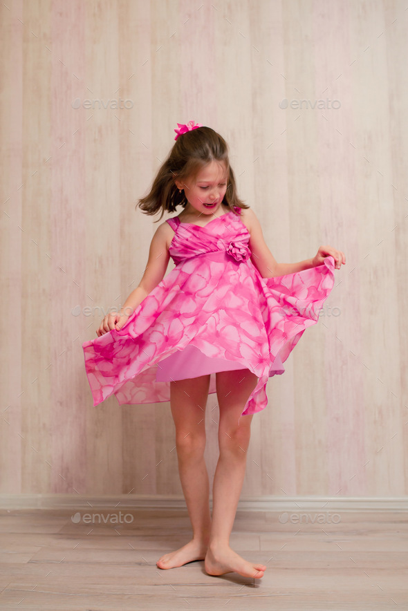 The girl tries on a pink dress with a rose and spins around at home.