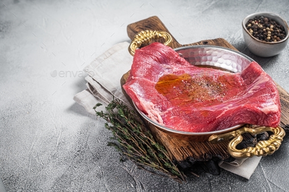 Flap or flank steak, raw beef meat in skillet with herbs and olive oil. White background. Top view.
