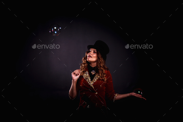 Woman magician illusionist circus with top hat in shows soap bubbles show at black background