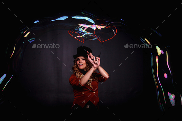 Happy woman magician illusionist circus with top hat in shows soap bubbles show at black background