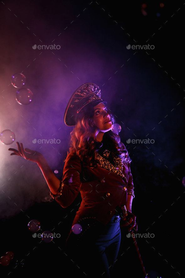 Female magician illusionist circus with stylish hat in shows soap bubbles show at black background