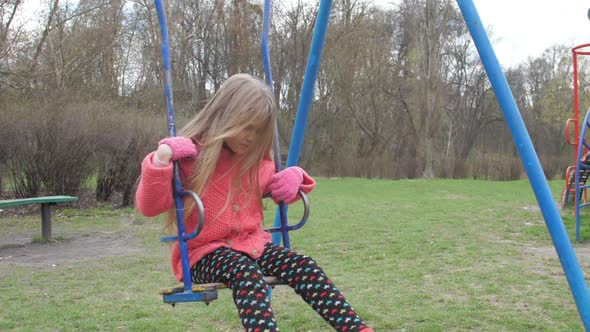 Sad Junior Schoolgirl with Long Fair Hair Sits on Blue Swing alt