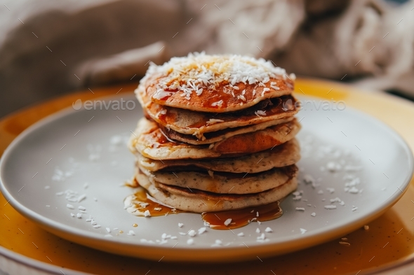 Banana pancakes with coconut flakes and maple syrup served on gray plate. Breakfast at home.