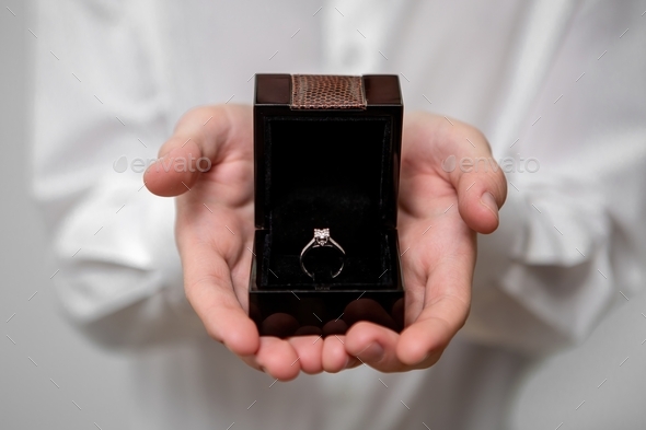 A young man is holding a gift, a jewelry box with a diamond ring. Marriage proposal, marry me
