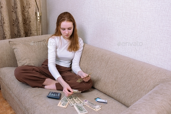 A young girl counts money, calculates her budget. The hostess sits at home on the couch and counts o