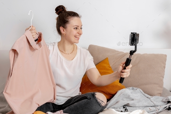 Young woman sitting on the bed at home and taking photo of her old clothes to sell them online.