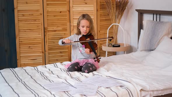 Child Girl Practicing Violin While Sitting on Bed alt