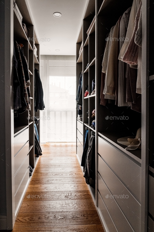 Walk in closet with hanged clothes and the window at the background, wooden floor, interior design