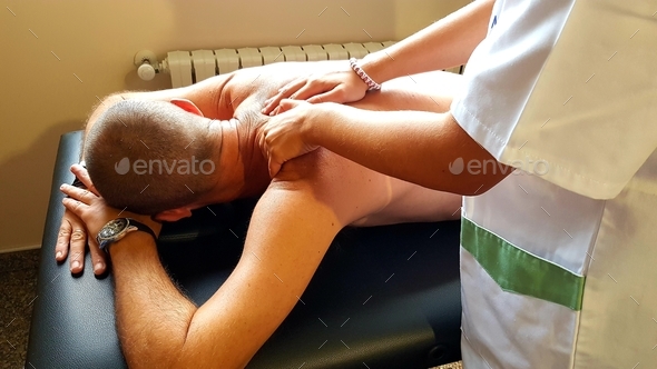 Female physical therapist assinting a patient giving treatment massaging the back and the shoulder
