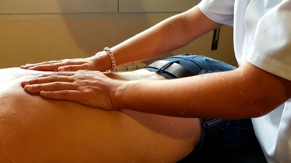 Female physical therapist assinting a patient giving treatment massaging the back and the shoulder,