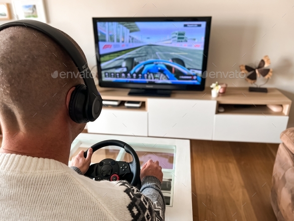 Man playing a video game at home; driving, steering wheel, car race, computer game on television - Stock Photo - Images