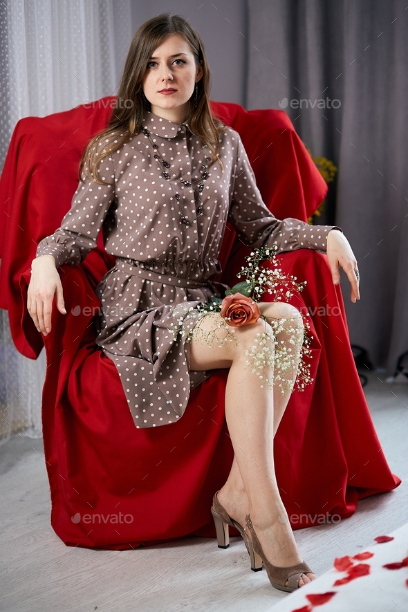 Stylish beautiful girl in red armchair in minimalist interior with red rose and gypsophila flowers.