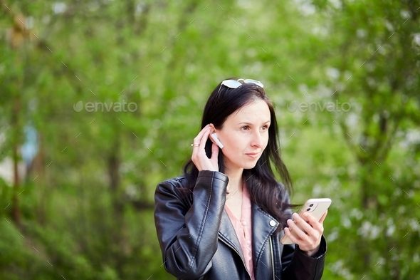 Young stylish woman using headphones and mobile phone outside.