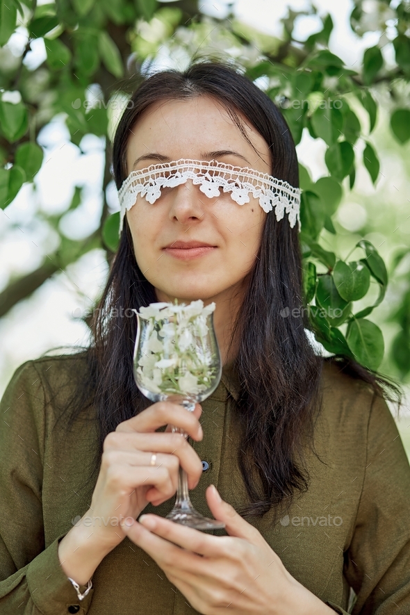 Young woman with closed eyes by lace holds wine glass full of blooming flowers
