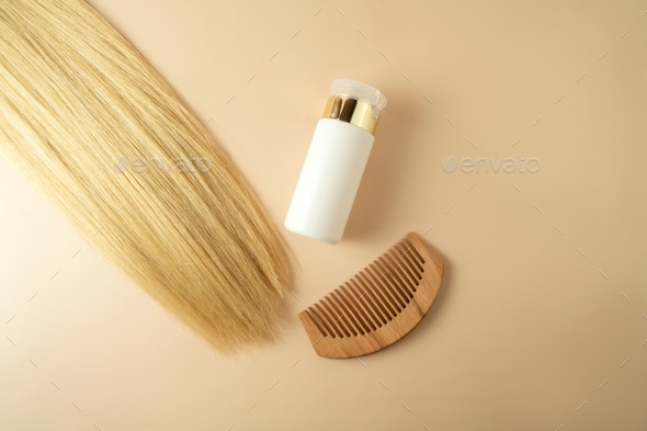 Blond hair and a hair serum and comb for extention lying on a beige background