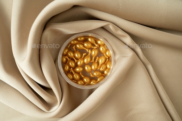 Golden capsules of the face serum or essential oil for face massage lying on a beige fabric