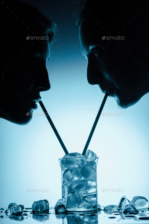 silhouettes of girls drinking cold water with ice cubes from one glass ...