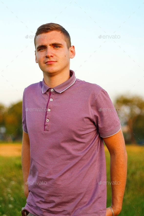 People walking. Portrait of serious young brunette man in purple polo shirt standing outdoor on natu