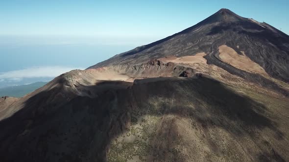 Aerial drone clip over the top of a volcano with clouds leaving shadows 