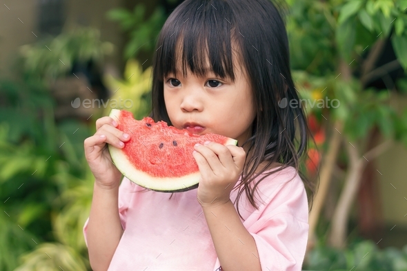 Happy Asian child girl eating and biting a piece of watermelon. Enjoy ...