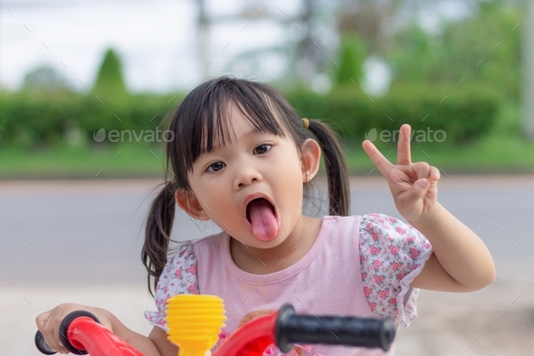 Face of smile and laugh Asian​ girl in head shot. Happy​ kid. A girl show Two fingers gesture.