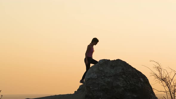 Silhouette of a Woman Hiker Climbing Alone on Big Stone at Sunset in Mountains alt