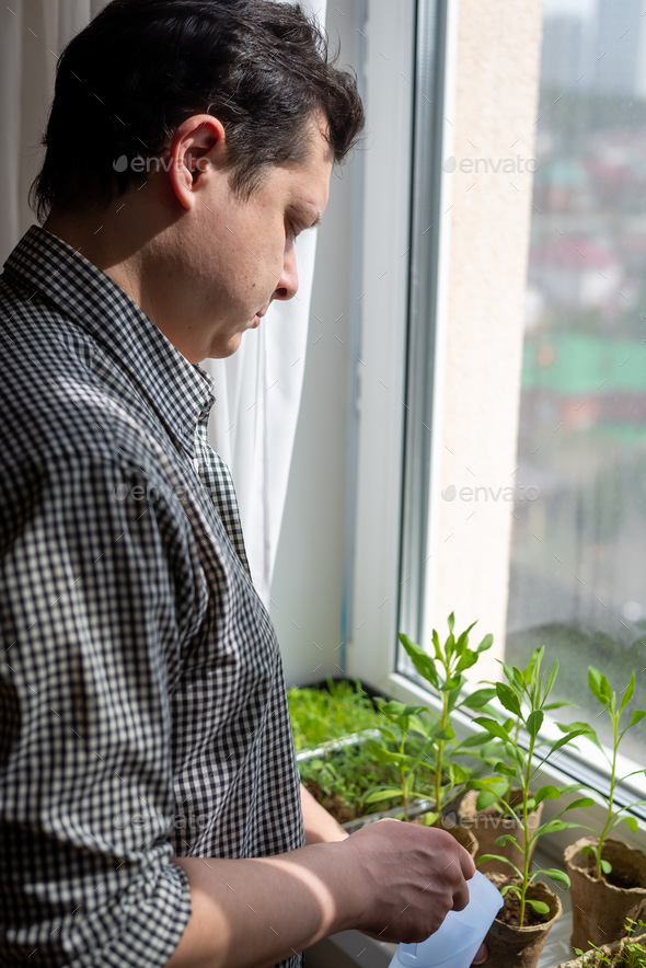 Home gardening, Young man doing household chores, watering seedlings plants flowers in eco pots