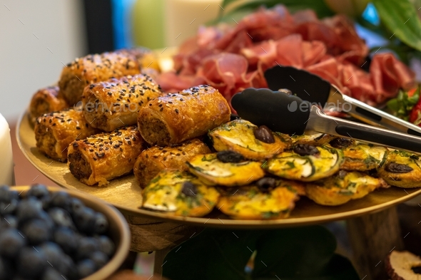 freshly baked sausage rolls and quiche's on a grazing table of food at a party