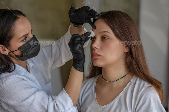 Eyebrow master stands in black clothes in front of the client and prepares for the dyeing procedure