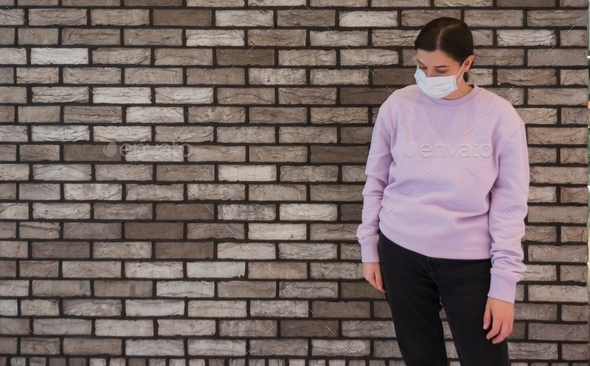 Woman in a medical mask a brick wall copy space in a sweatshirt in Pantone Color of the Year 2022