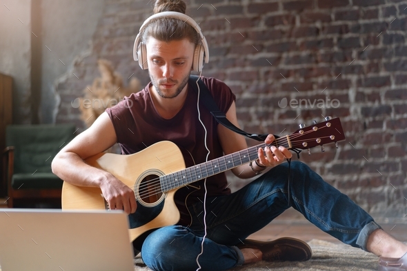 Young Handsome Man watching guitar tutorial on laptop Online courses guitar playing